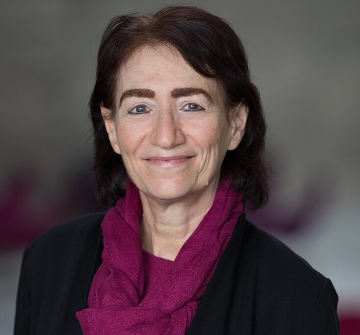 A Caucasian woman smiling at the camera. She's wearing a black top with a magenta scarf. 
